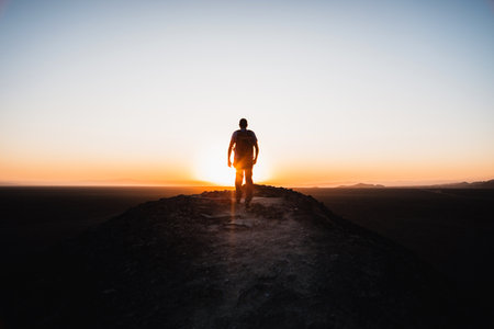Rear view of young silhouette hiker walking on the mountain at sunset.