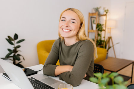 Young woman with laptop smiling at camera at homeの写真素材