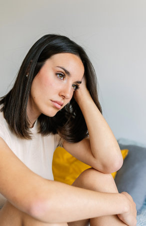 Portrait of young adult woman feeling sad sitting on bed feeling sad at homeの写真素材