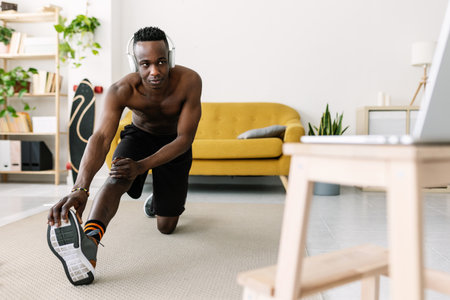 Young adult african man training and stretching while watching fitness video