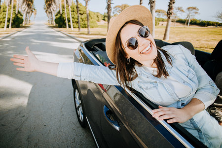 Happy young woman enjoying freedom on travel trip by cabriolet carの写真素材