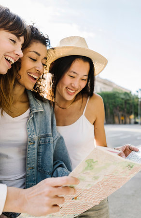 Three beautiful young adult women looking at city map while sightseeing