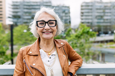 Cheerful portrait of positive aged woman smiling at camera standing at city
