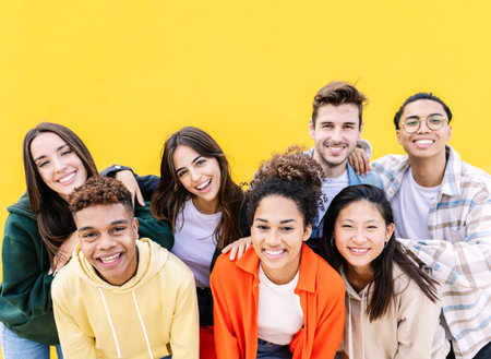 Group portrait of young multiethnic student friends against yellow wallの写真素材