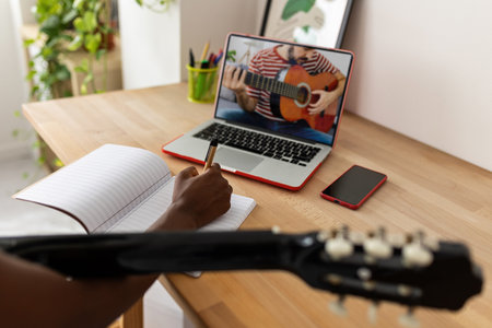 African teenage girl watching online course on laptop while playing the guitarの写真素材