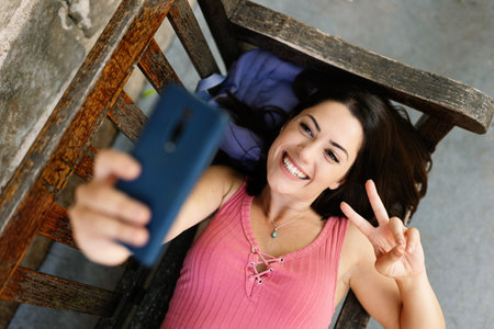 Beautiful caucasian woman taking selfie portrait with phone lying on bench parkの写真素材