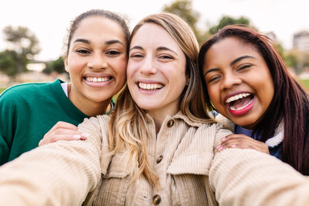 Young group of three diverse cheerful women taking selfie together outdoors