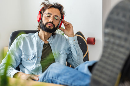 Young man with closed eyes enjoying music with headphones in the office.の写真素材