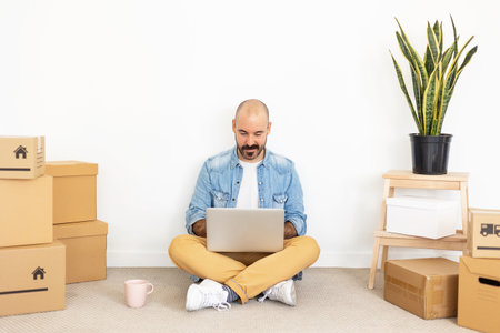 Hipster young adult man using laptop in new home