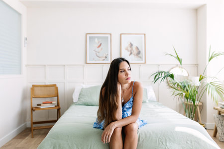 Sad young adult woman sitting on bedの写真素材