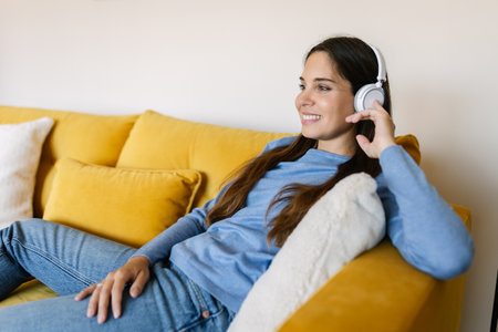 Happy young woman listening to music relaxing on sofa in the living room at homeの写真素材