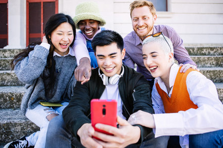 Happy group of young people having fun using mobile phone together outdoorsの写真素材