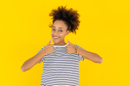 Excited young african woman showing thumbs up with hand over yellow backgroundの写真素材