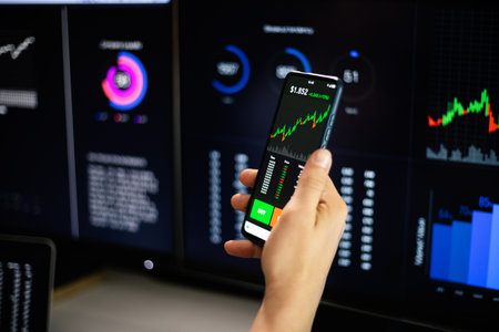 Stock trader analyzing charts on mobile phone and multiple computer screensの写真素材