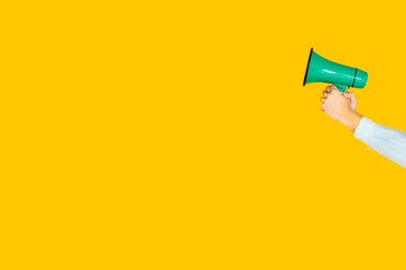 Hand holding green megaphone on yellow background promoting an eventの写真素材