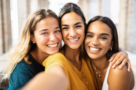 Three young friends laughing together taking selfie outdoorsの写真素材