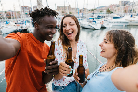 Three happy multiracial friends drinking beer while taking selfie on boat partyの写真素材
