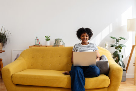 Young happy black woman using laptop computer relaxing on sofa at homeの写真素材