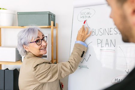 Middle aged businesswoman pointing marker to whiteboard on presentationの写真素材