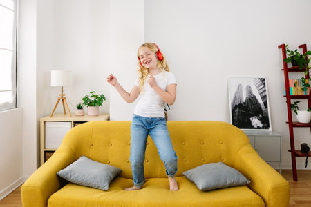 Little girl having fun dancing on sofa while listening musicの写真素材