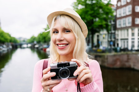 Portrait of happy young woman holding photo camera over Amsterdam canal.の写真素材