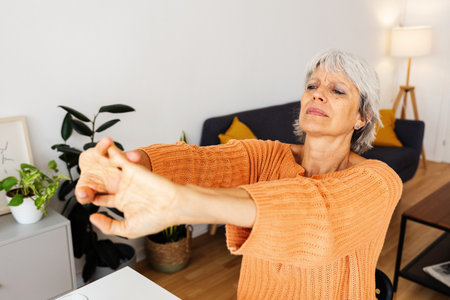 Senior 50s woman stretching arms at home office deskの写真素材