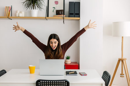 Happy beautiful woman celebrating success after reading message on laptopの写真素材