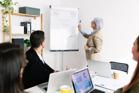 Senior businesswoman explaining business plan on whiteboard to colleaguesの写真素材