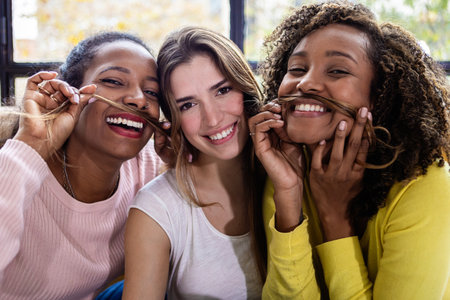 Three playful young women making fake mustaches with hair