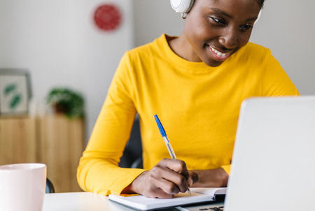 Smiling african woman student using laptop computer for online learning at homeの写真素材