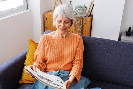 Senior adult woman reading newspaper relaxing on sofa at home