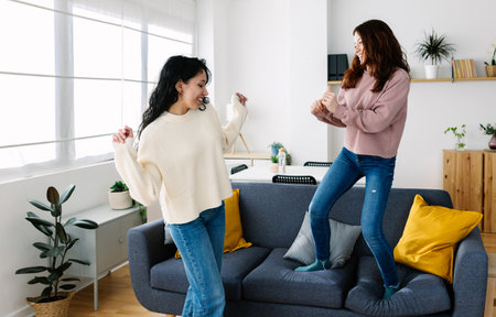 Happy young female friends having fun dancing together at home