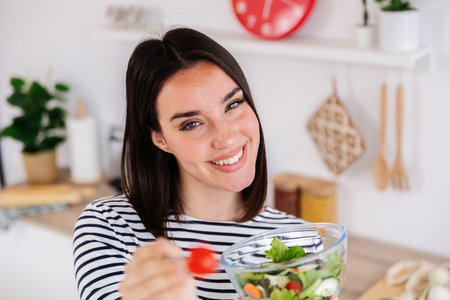 Young happy woman eating fresh salad in modern kitchen at homeの写真素材