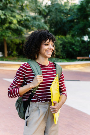 Young happy student girl with backpack standing at college campus