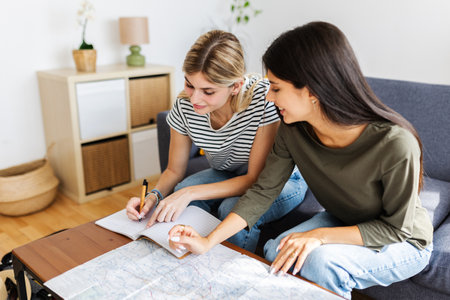 Two happy young girls planning their next vacation trip at homeの写真素材