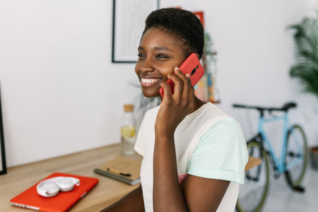Smiling freelancer talking on phone at home office deskの写真素材