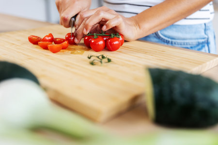 Woman chopping cherry tomatoes on cutting board, preparing salad in kitchenの写真素材