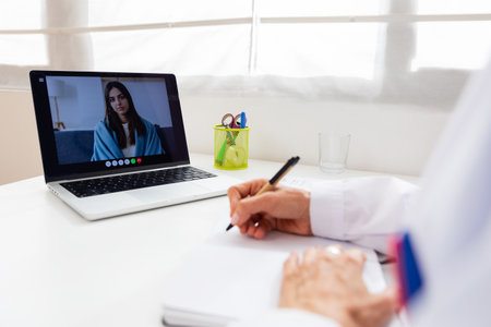 Rear view of senior doctor talking with female patient through video callの写真素材