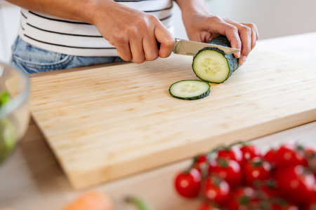 Close up woman hands slicing fresh cucumber on wooden cutting board in kitchenの写真素材