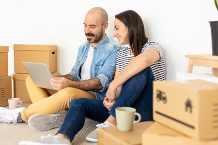 Happy young adult couple using laptop computer in new homeの写真素材