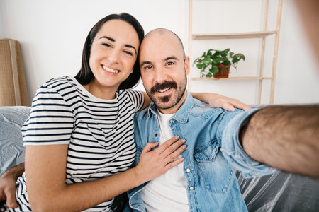 Happy young couple taking selfie with mobile phone after moving to new homeの写真素材