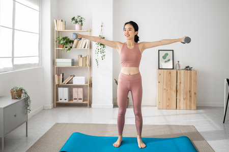 Young adult asian woman doing exercises with dumbbells in the living roomの写真素材