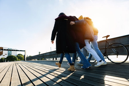 Friends walking together on bridge in winter sunlightの写真素材