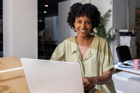 Smiling woman working on laptop in modern bright officeの写真素材