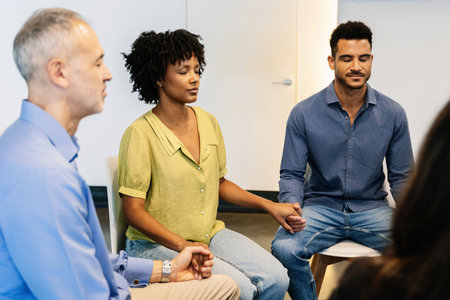Diverse group of people holding hands with eyes closed during therapy sessionの写真素材