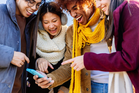 Multiracial friends laughing together watching social media content on phoneの写真素材