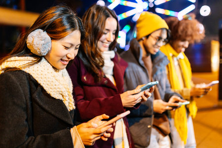 Happy millennial people using smart phones devices together outdoors on winter.の写真素材