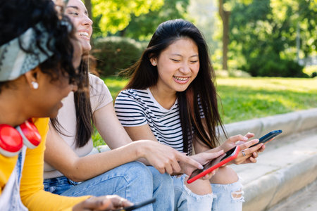 Three happy women using mobile phones at parkの写真素材