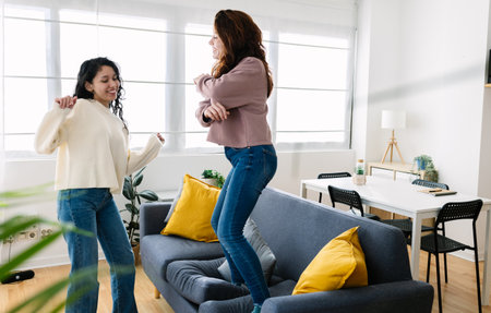 Two happy woman friends having fun dancing on sofa at home party