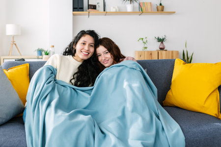 Two young women watching TV covered with blanket on winter at homeの写真素材